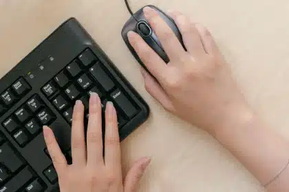 Mani anonime che digitano su una tastiera illuminata, con pattern di codice sullo sfondo scuro