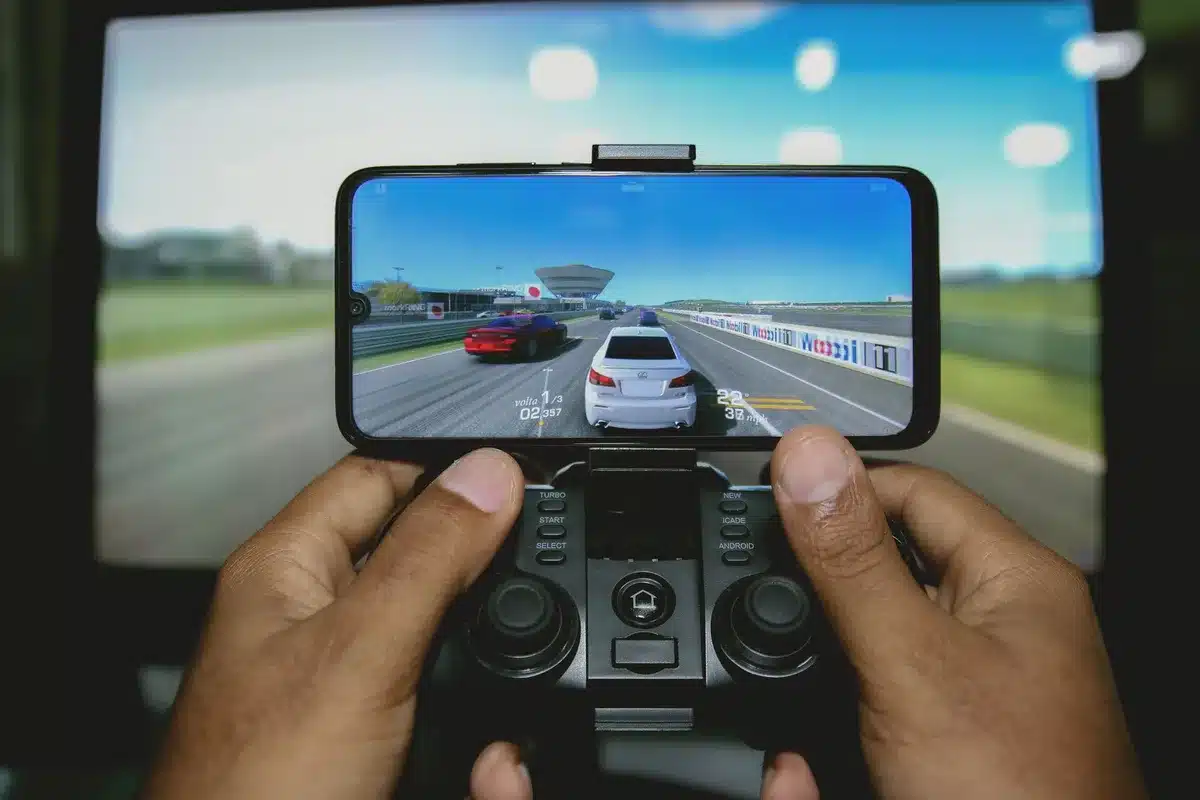 Mani di un giocatore su un controller con schermo illuminato sullo sfondo