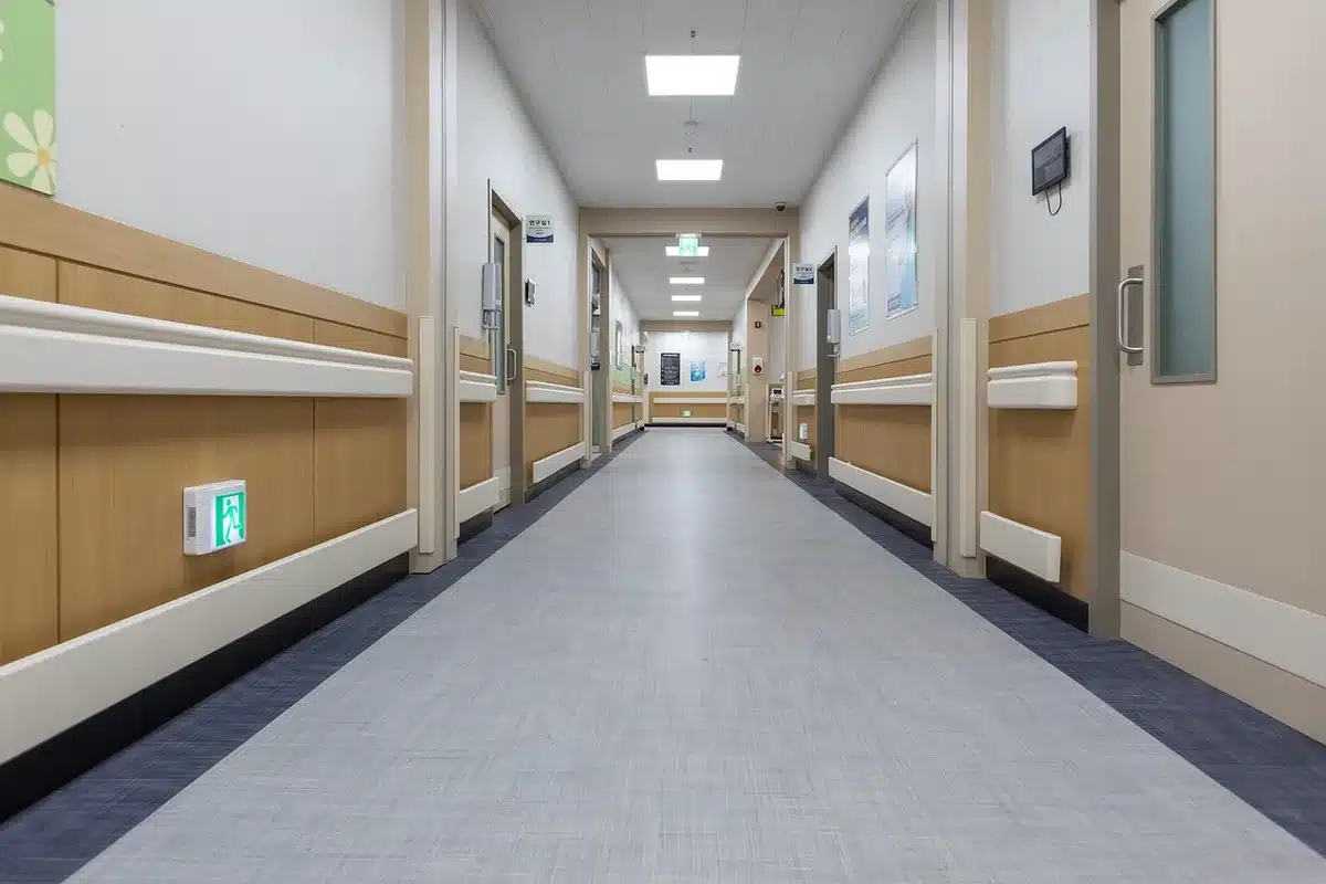 Corridoio d'ospedale con una barella e una porta rotta che suggerisce violenza