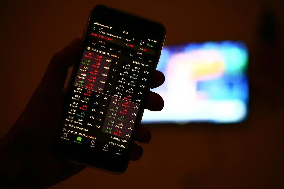 Mani anonime che tengono uno smartphone con un'interfaccia app, laptop e grafici sullo sfondo