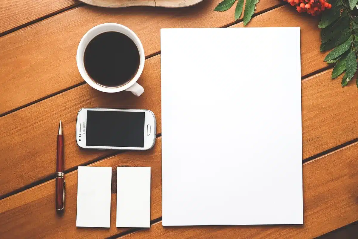 Mani che tengono uno smartphone su una scrivania con valigia e cuffie sullo sfondo