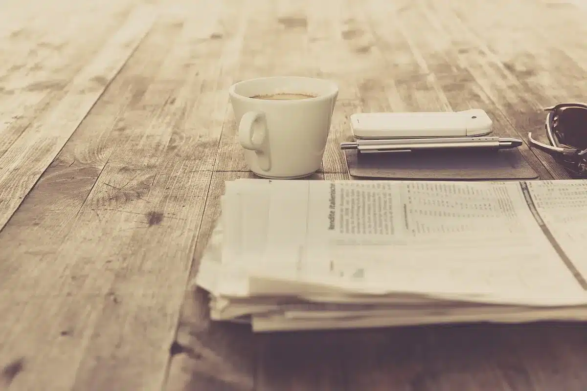 Mano con smartphone su tavolo con auricolare e tazza di caffè